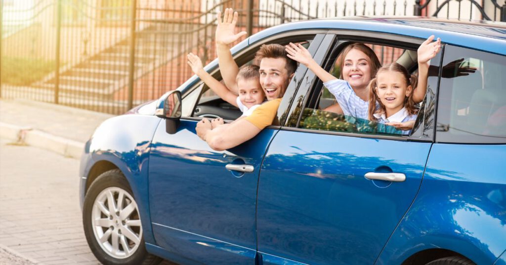 una familia dentro de un coche azul, se despide al salir de viaje